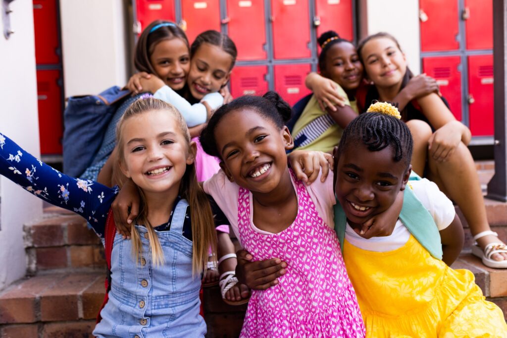 Portrait of diverse happy schoolgirls embracing in elementary school cloakroom